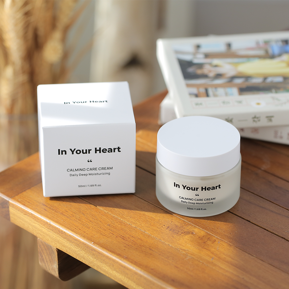 A jar of 'In Your Heart Calming Care Cream' next to its elegant white box on a wooden table.