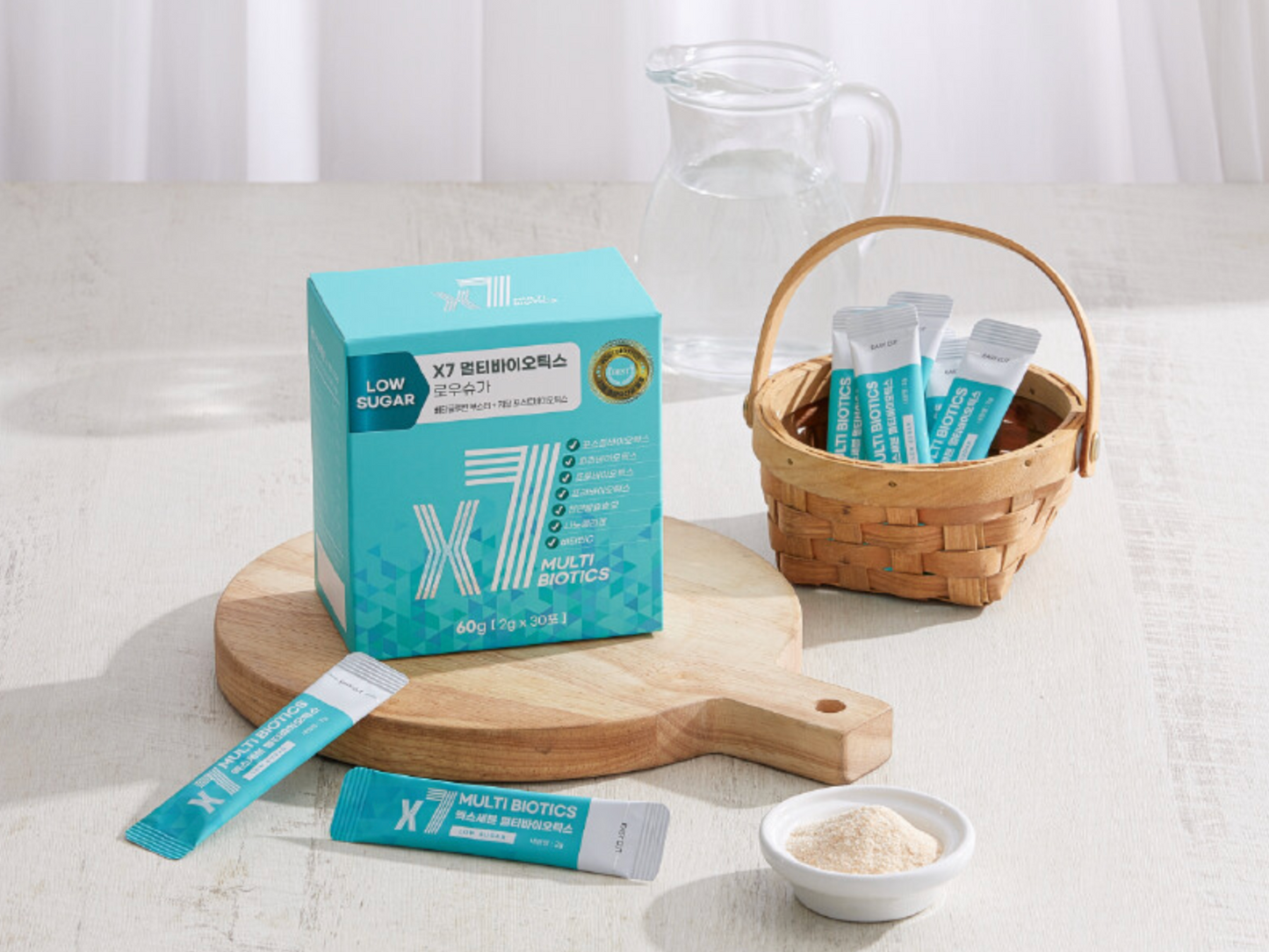 A wooden serving board with a teal box of X7 Low Sugar Multi Biotics, a wicker basket holding sachets, and a small white bowl containing powdered supplement placed next to individual teal satchets.