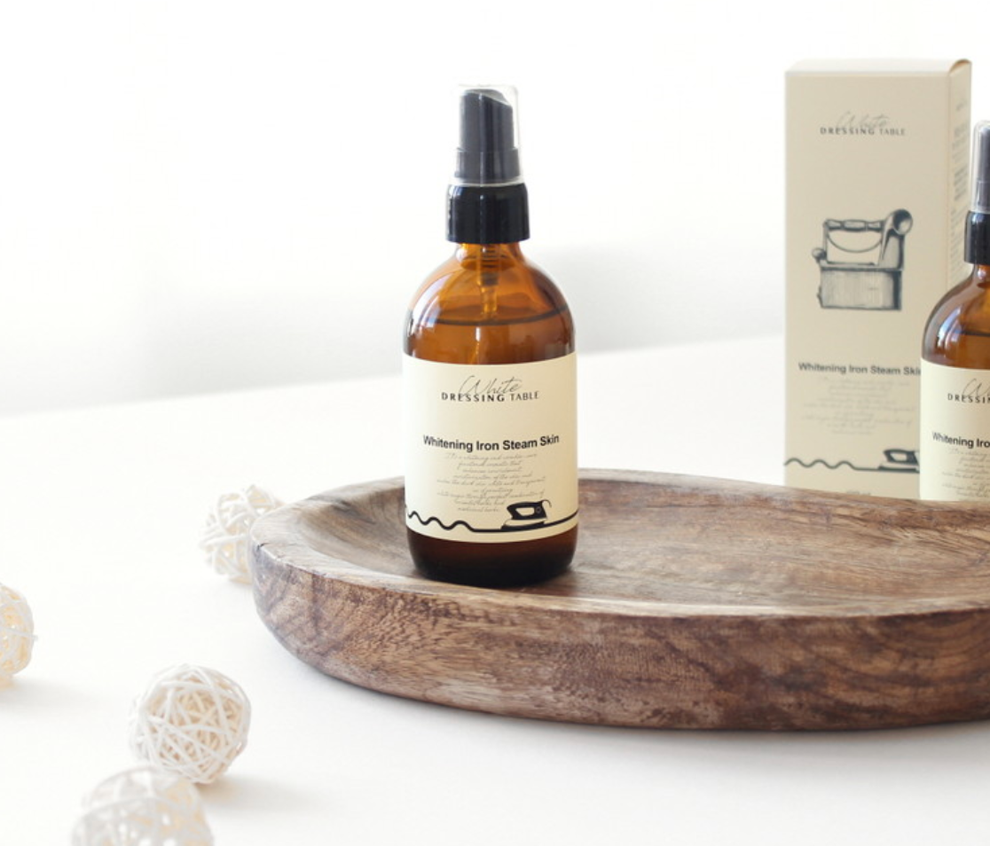 DRESSINGTABLE Brightening Iron Steam Skin toner mist in amber bottle on wooden tray with decorative spheres.