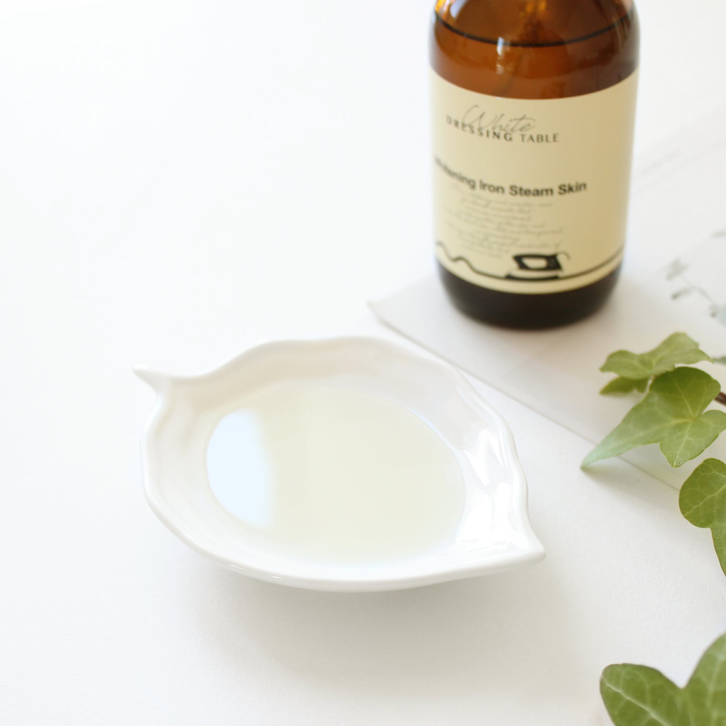 DRESSINGTABLE Brightening Iron Steam Skin toner bottle next to a white dish with liquid, enhancing skincare routine.