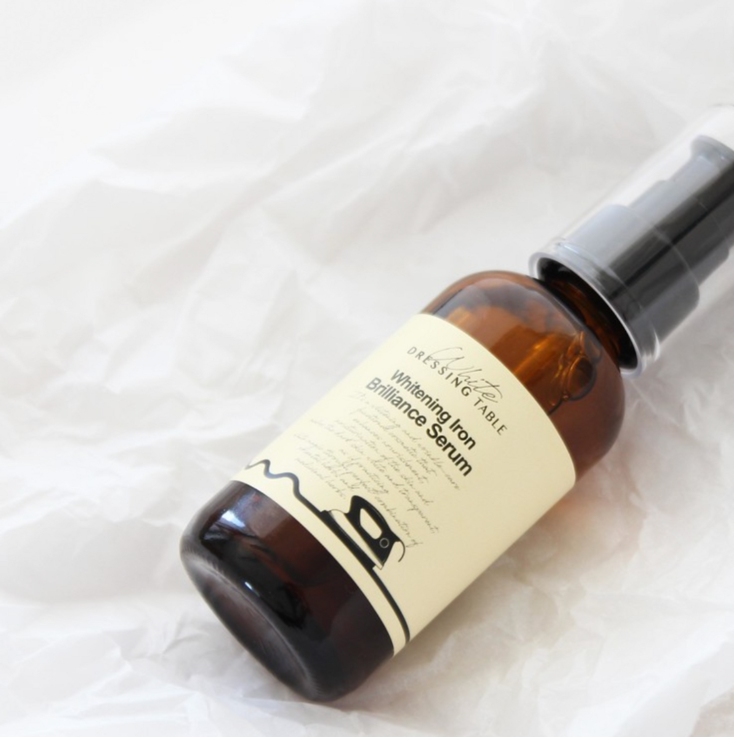 DRESSINGTABLE Brightening Iron Brilliance Serum in a sleek glass bottle on crumpled paper background.