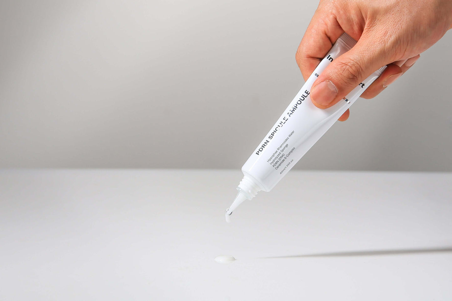 Hand holding IN YOUR HEART PDRN Spicule Ampoule tube, dispensing product on table surface.