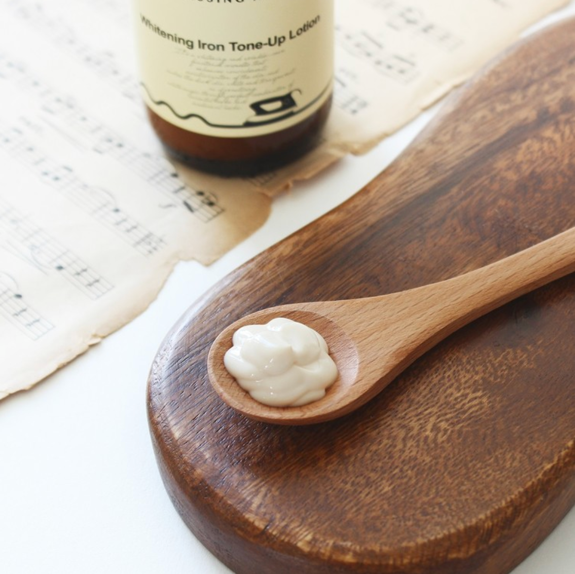 DRESSINGTABLE Brightening Iron Tone-Up Lotion on a wooden spoon with musical sheet background.