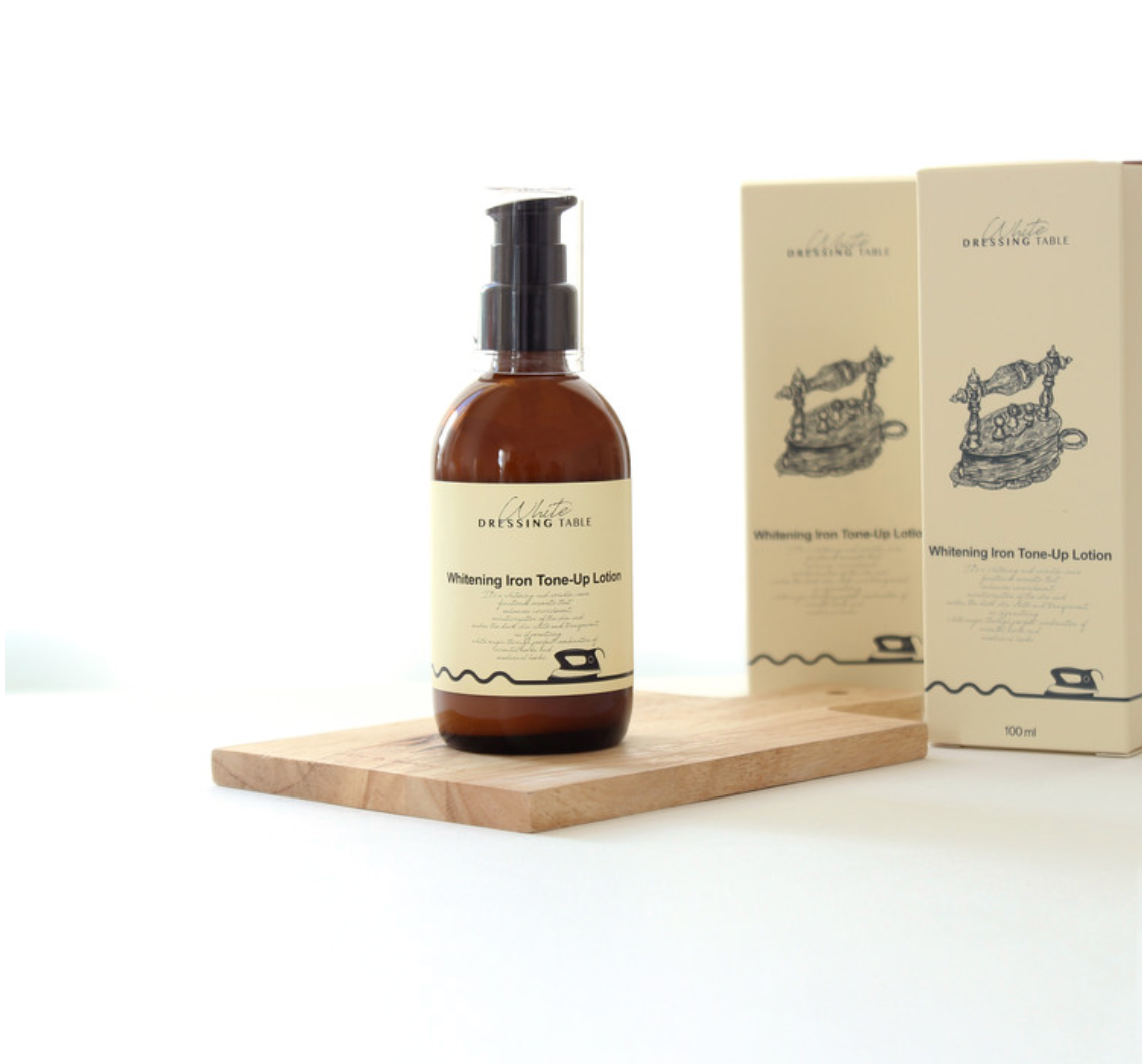 DRESSINGTABLE Brightening Iron Tone-Up Lotion in a bottle on a wooden surface next to its box packaging.