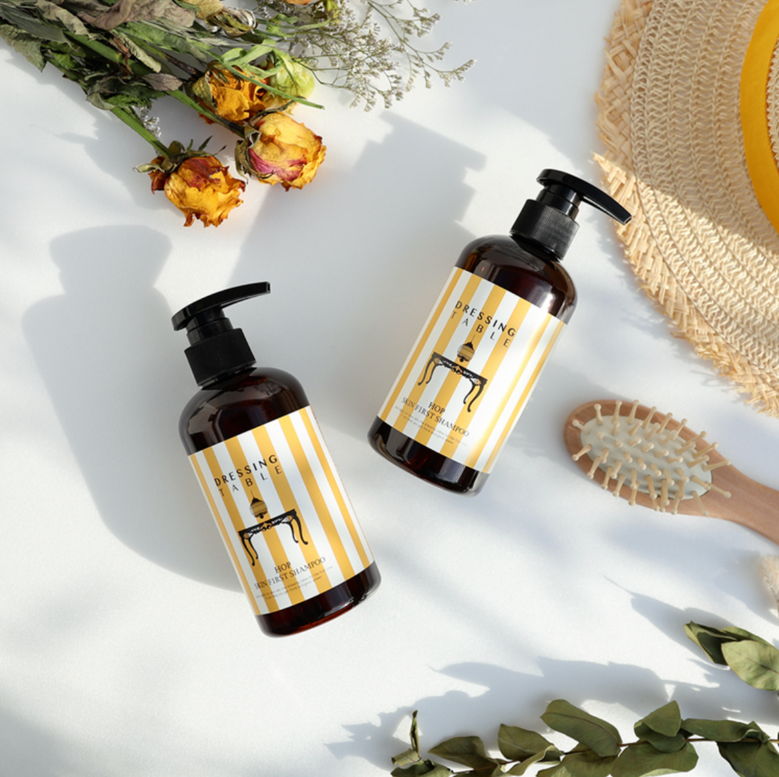 two amber bottles with black pumps next to brush and yellow dried roses