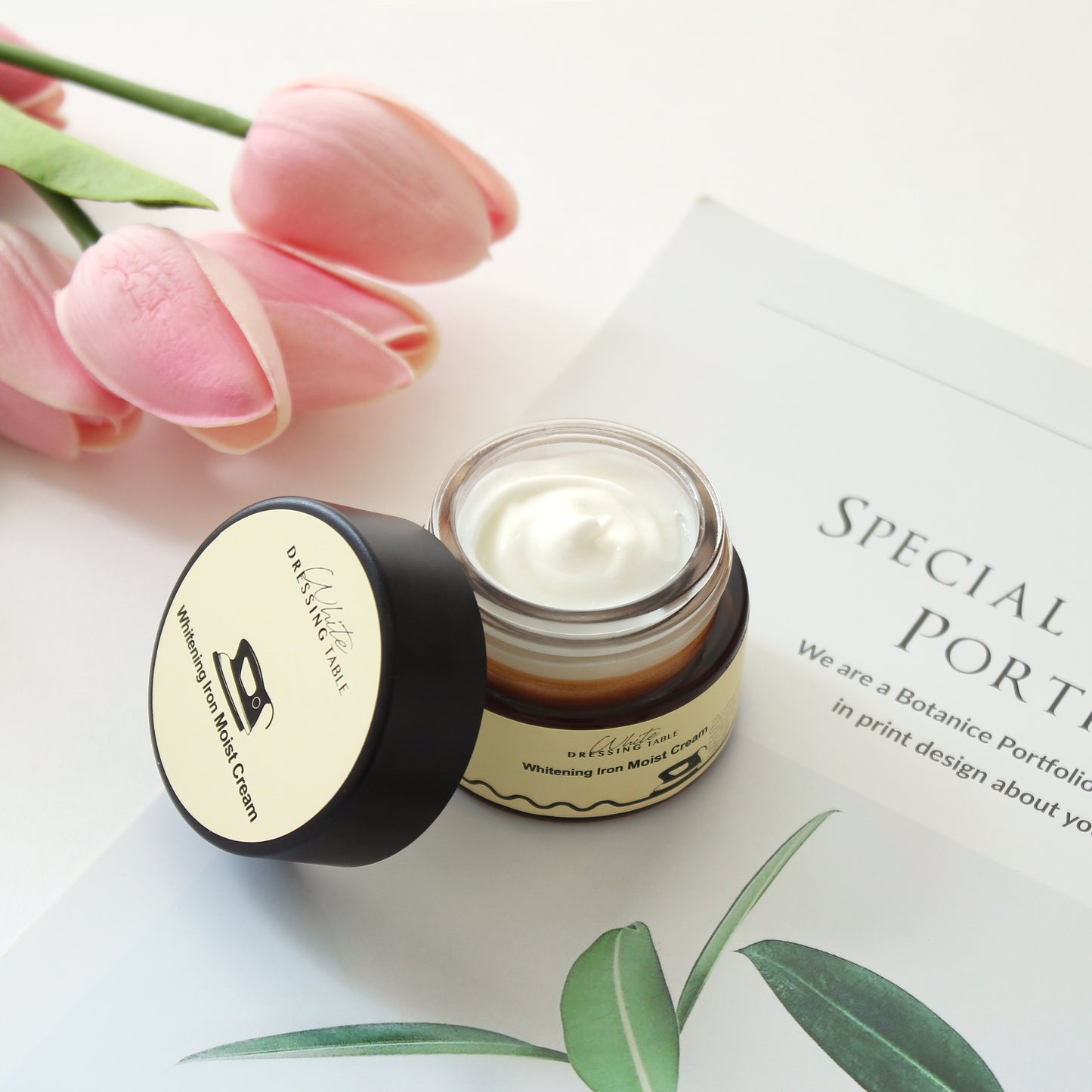 DRESSINGTABLE Brightening Iron Moist Cream in a jar with tulips and magazine on a table.