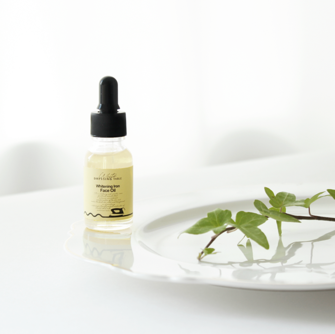 DRESSINGTABLE Brightening Iron Face Oil in a dropper bottle on a plate with green leaves.