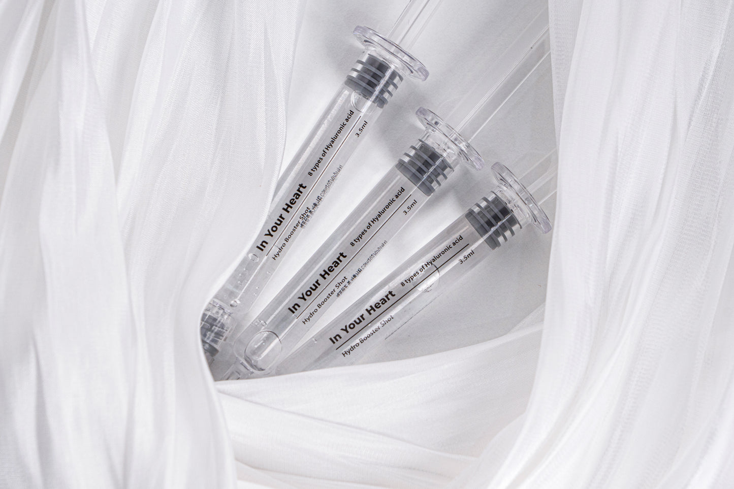 Three IN YOUR HEART Hydro Booster Shot ampoules nestled in soft white fabric.