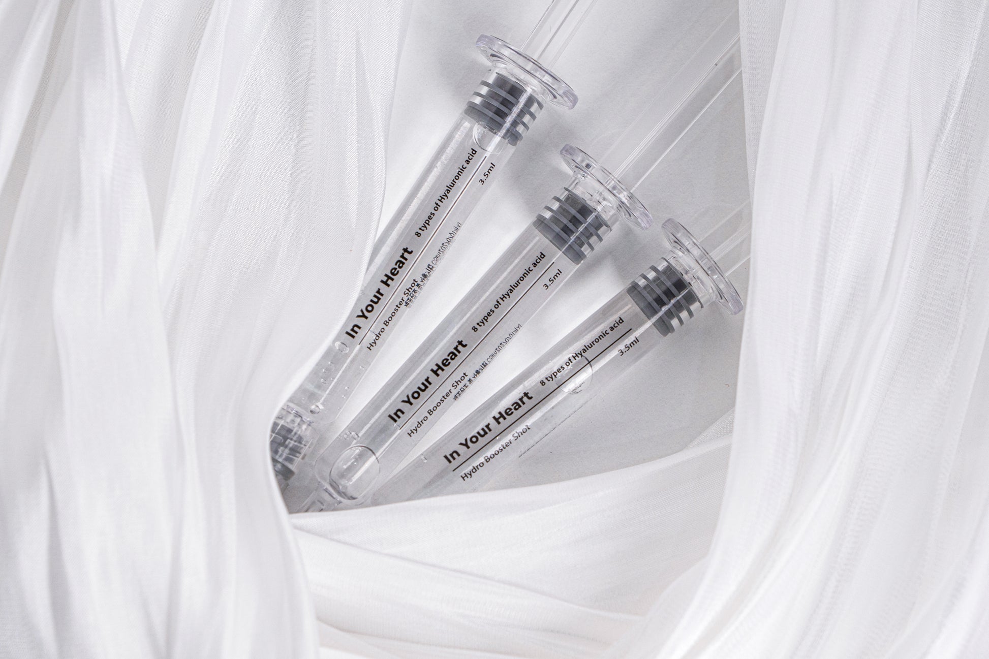 Three IN YOUR HEART Hydro Booster Shot ampoules nestled in soft white fabric.