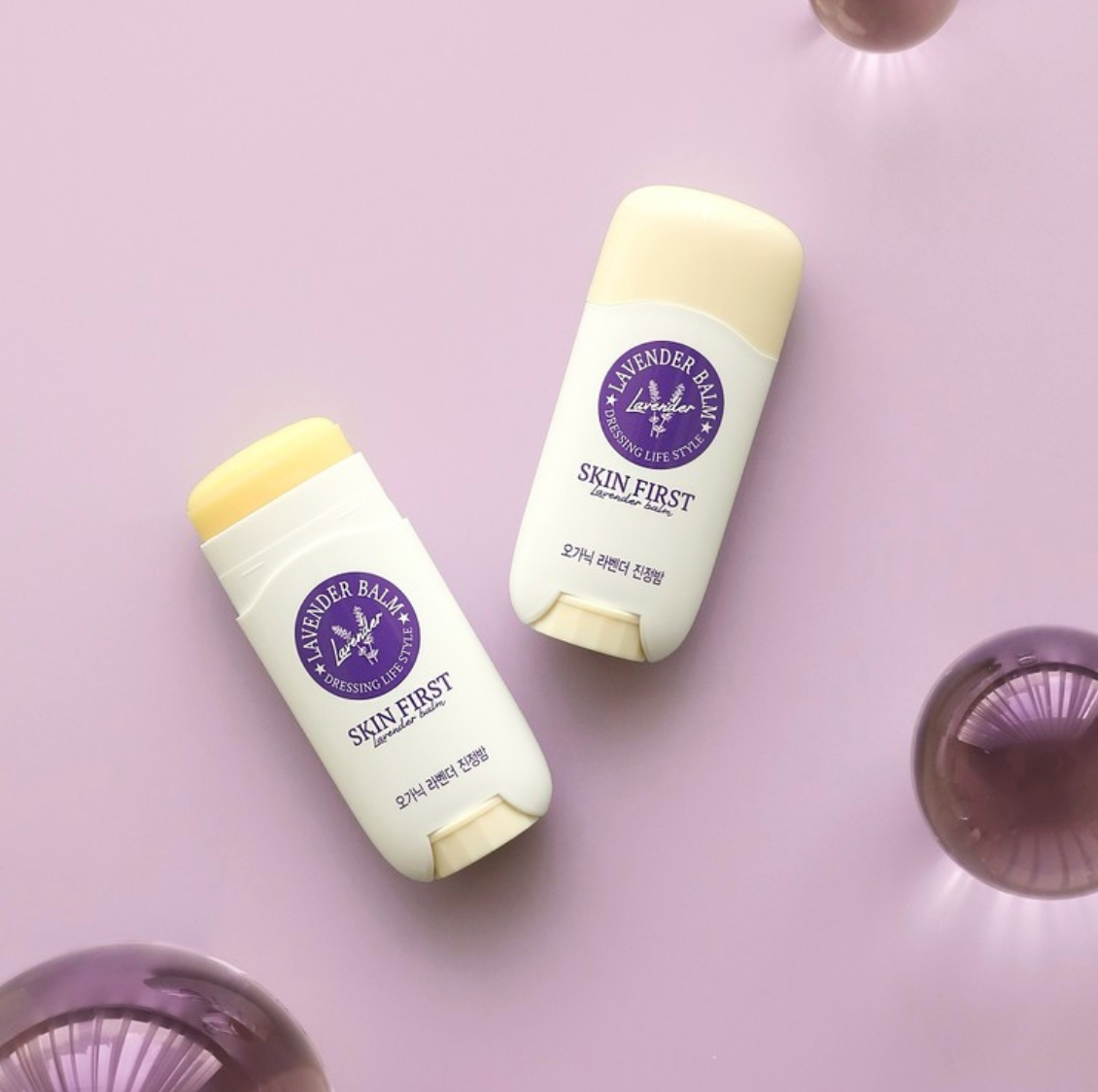 Two DressingTable Skin First Lavender Soothing Balm Sticks against a pastel lavender background, one with the balm extended, emphasizing its smooth and easy-to-apply texture