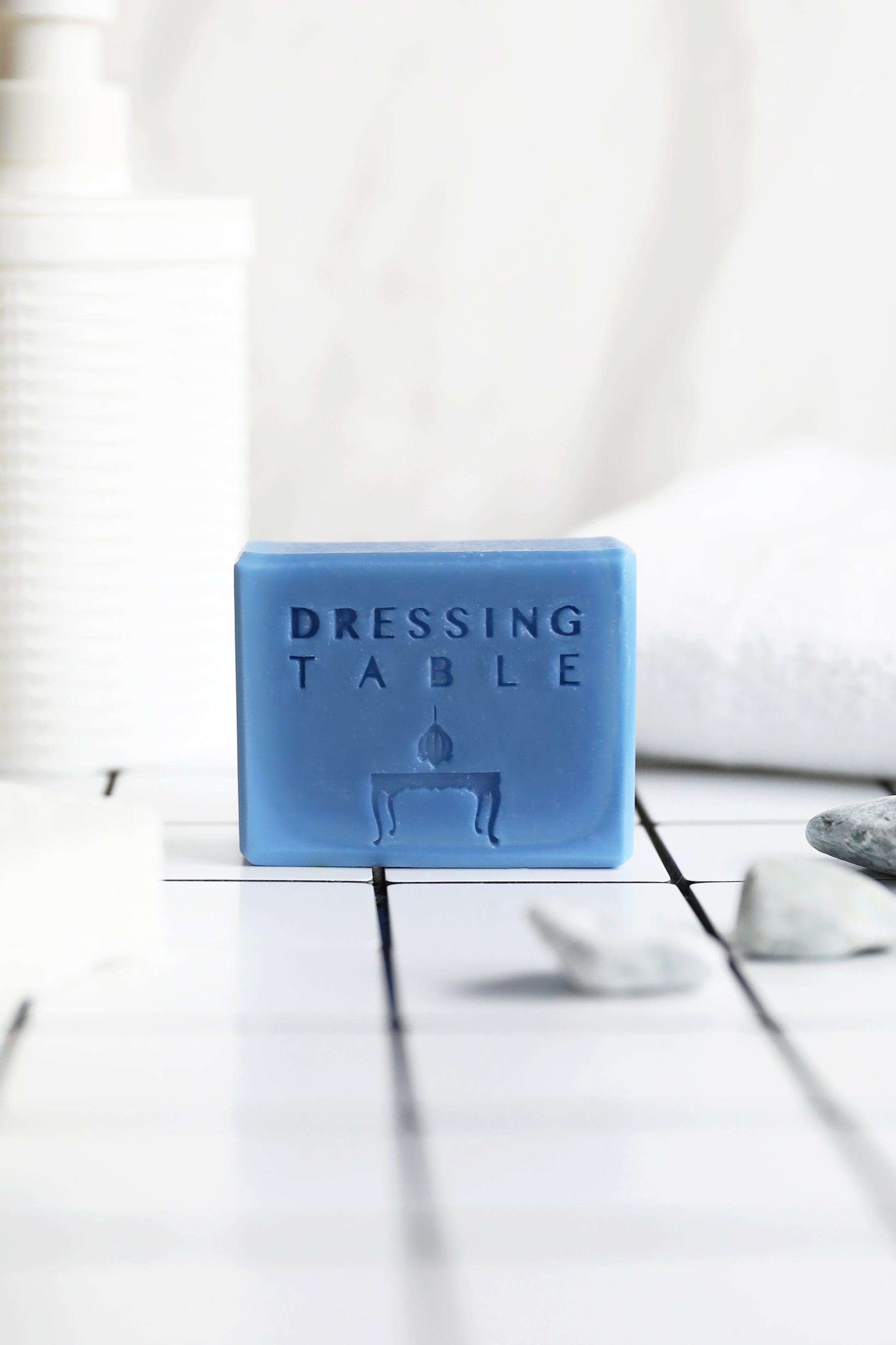 Blue colored bar soap with "dressing table" written on it on white tiles next to some rocks