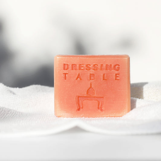 Salmon pink colored bar soap with "dressing table" written on it, on top of white towel.