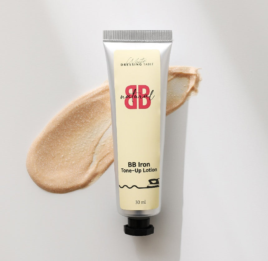 Silver bottle of bb lotion with peach liquid swatch behind it