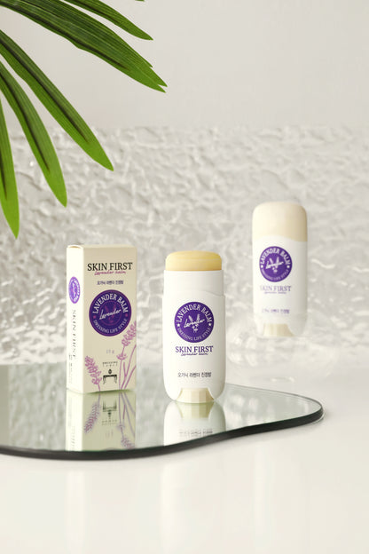 DressingTable Skin First Lavender Soothing Balm Stick placed on a reflective surface with its packaging in the background, showcasing the sleek, travel-friendly design and soft cream color.