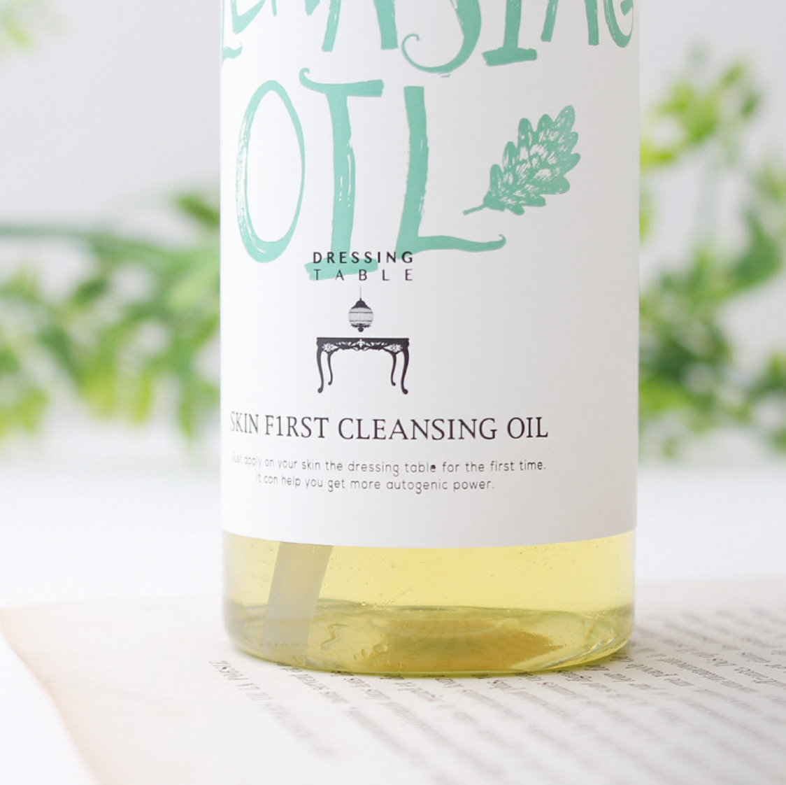 A focused image of the [DressingTable] Skin First Cleansing Oil bottle, highlighting its stylish packaging with green and white labeling, surrounded by soft natural elements in the background.