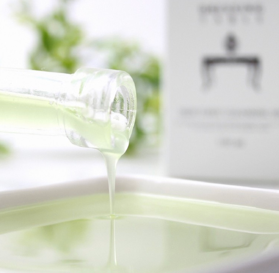 A detailed shot of the light green cleansing oil being poured from a glass bottle, showcasing its smooth texture and luxurious consistency.