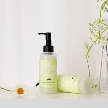 Two bottles of [DressingTable] Tea Tree Pore Cleansing Gel, one standing upright and the other lying on its side, displayed with greenery and a white daisy on a clean, bright surface.