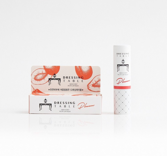 A tube of DressingTable Plum Lip Balm standing upright next to its packaging, featuring a white and orange design with plum graphics.