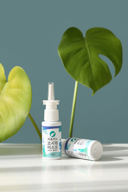 Two Phytoncide Nasal Mist Spray bottles (30ml) are placed on a reflective surface, with a green plant in the background. One bottle stands upright while the other is lying on its side, highlighting the product's compact and portable design.