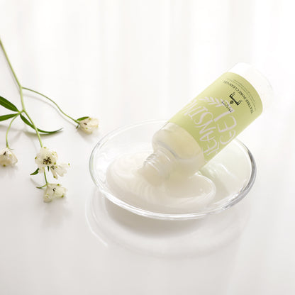 Tea Tree Pore Cleansing Gel tilted to pour the gel into a transparent glass dish, surrounded by delicate white flowers on a glossy white background.