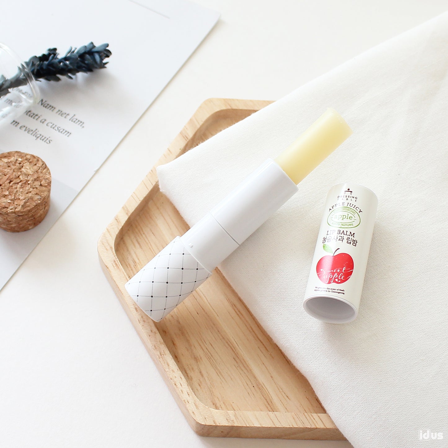 Apple Lip Balm displayed on a wooden tray with its cap removed. The balm is accompanied by a soft white cloth and natural decor, creating a cozy and clean aesthetic.