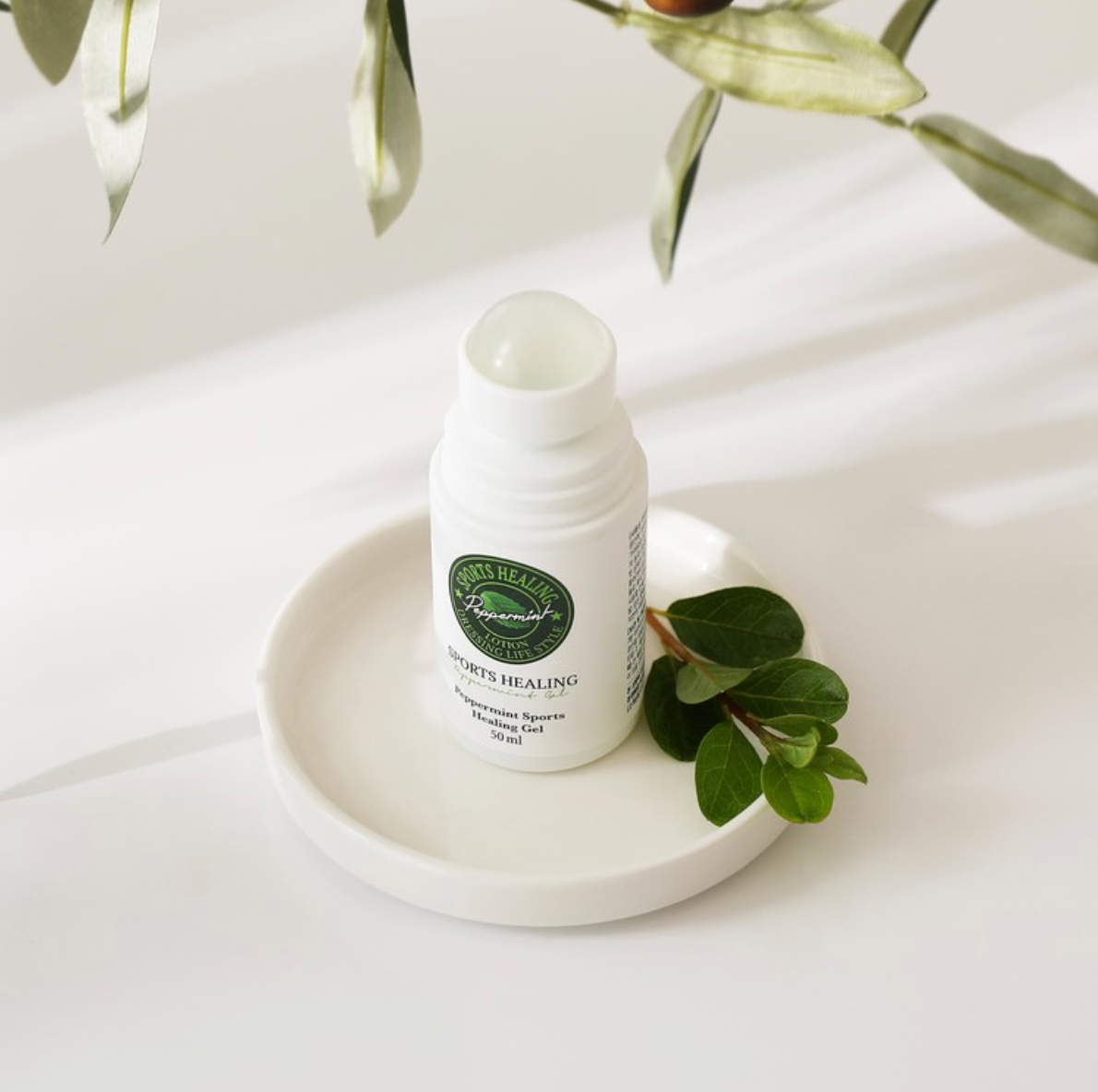 Open DressingTable Sports Healing Gel bottle displayed on a white ceramic dish, surrounded by fresh green leaves and bathed in soft natural light