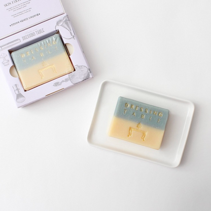 two green and yellow bar soaps; one in box and another on a white tray