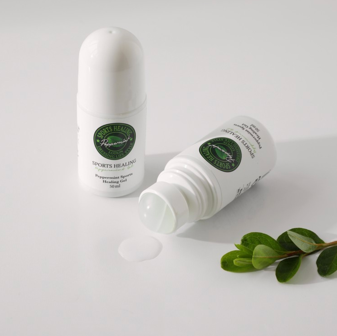 Two bottles of DressingTable Sports Healing Gel, one open showing the gel's clear texture, styled with green foliage on a clean white surface