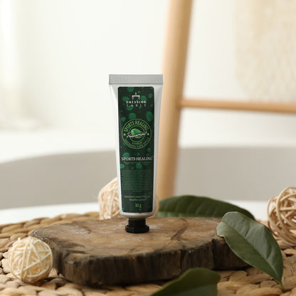 Sports Healing Lotion tube (30g) displayed on a rustic wooden platform surrounded by natural decorative elements, highlighting the product’s organic and therapeutic essence.