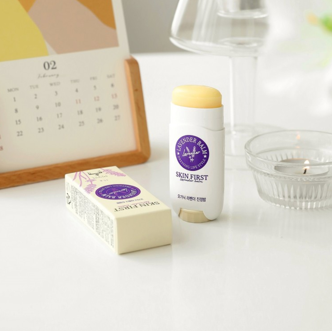 DressingTable Skin First Lavender Soothing Balm Stick with its packaging on a white desk, accompanied by a candle and a calendar, reflecting a serene and natural vibe.